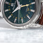 Close-up of the Grand Seiko Automatic GMT Elegance wristwatch with a Mount Iwate dial in British Racing Green and a brown leather strap, displayed on paper featuring Japanese text.