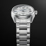 The Grand Seiko Spring Drive 5 Days Evolution 9, featuring a textured white dial and stainless steel bracelet, is elegantly displayed against a dark gradient background.