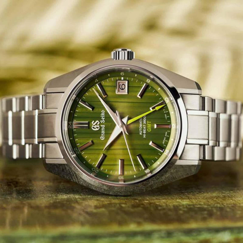 The Grand Seiko Hi-Beat GMT Heritage features a green textured dial inspired by bamboo garden paths, a date window at 3 o’clock, silver hour markers, and stainless steel bracelet, powered by the precise Hi-Beat Caliber 9S86.