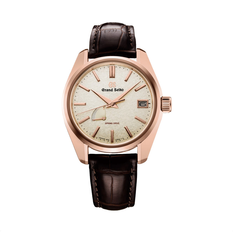 The Grand Seiko Spring Drive Heritage Limited Edition wristwatch features a light textured dial, gold-tone case, date at 3 o’clock, and a dark brown leather strap, displayed against a white background.