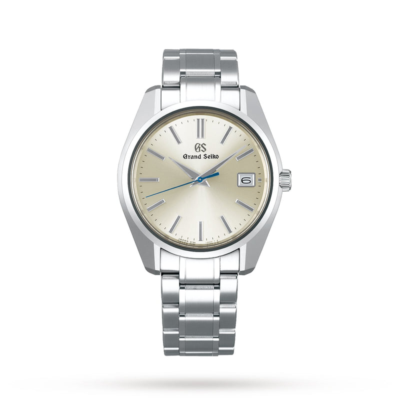 The Grand Seiko Quartz Heritage wristwatch features a cream dial, blue seconds hand, silver hour markers, Calibre 9F85 movement, date at 3 o’clock, and Zaratsu-polished metal link bracelet, displayed against a white background.