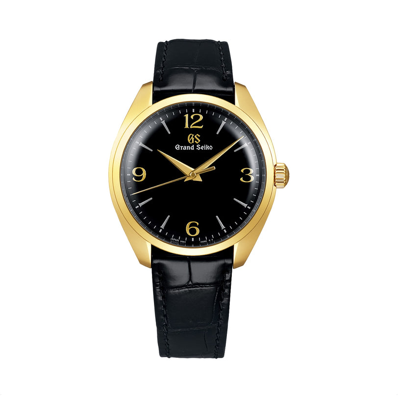 The Grand Seiko Manual Elegance wristwatch features a gold case, black dial with gold numerals, and a black leather strap, showcasing refined Japanese aesthetics on a white background.