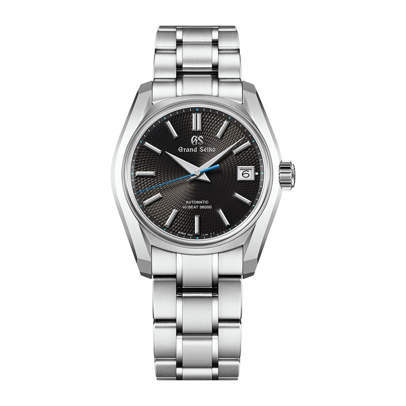 The Grand Seiko Hi-Beat Heritage is a stainless steel wristwatch with a black textured dial inspired by Jodogahama beach, silver indices, date at 3 o’clock, and a metal link bracelet.