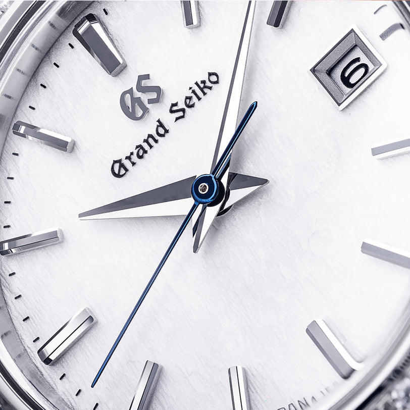 Close-up of a Grand Seiko Ladies Heritage watch face with silver hour markers, blued steel seconds hand, a date window at 6 o’clock, and a textured snowflake dial.