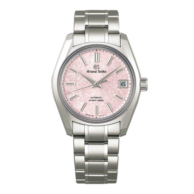 The Grand Seiko Hi-Beat Heritage features a stainless steel case, pink textured dial, silver hour markers, date at 3 o’clock, and hi-beat 9S85 movement on a metal bracelet.