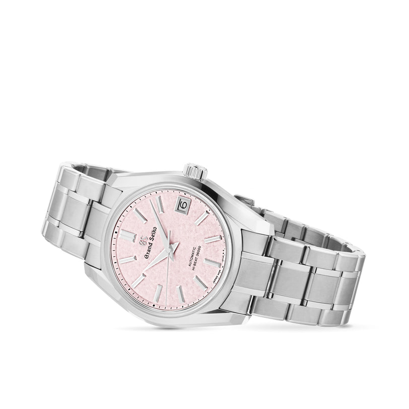 The Grand Seiko Hi-Beat Heritage is a stainless steel watch with a pink textured dial, date at 3 o’clock, silver hour markers, 9S85 movement, and a three-link metal bracelet, shown on a white background.