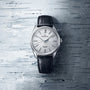 A Grand Seiko Manual Hi-beat 80 Hours Evolution 9 wristwatch with a textured white birch dial and black leather strap, shown on a gray patterned surface.