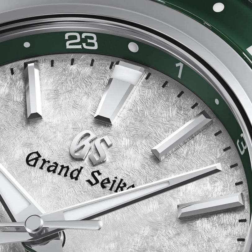 Close-up of the Grand Seiko Hi-Beat GMT Sport watch face, featuring a textured white dial, silver hour markers, and a green bezel set to 23, showcasing its GMT function.