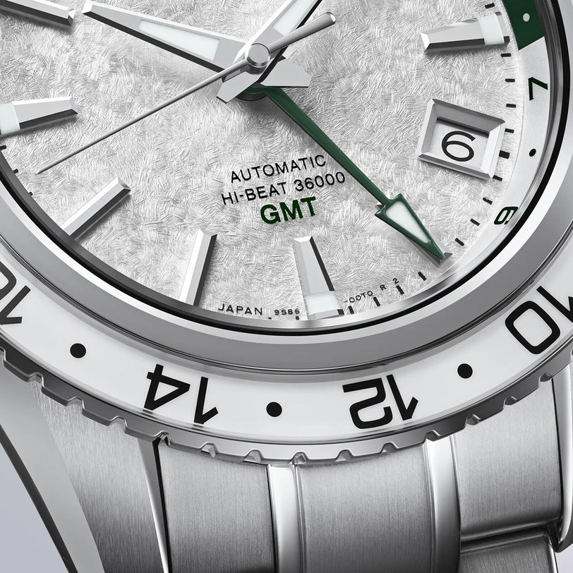 Close-up of the Grand Seiko Hi-Beat GMT Sport, highlighting its textured dial with “Automatic Hi-Beat 36000 GMT” text, green GMT hand, and part of the metal bracelet from the Sports Collection.