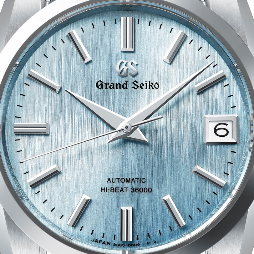 Close-up of the Grand Seiko Hi-Beat Heritage watch showing its light blue textured dial, silver markers, and a date window at 3 o’clock.