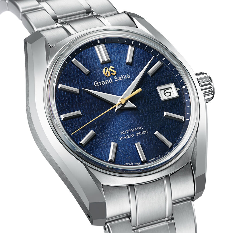 The Grand Seiko Hi-Beat Heritage is a stainless steel watch with Zaratsu polishing, a blue textured dial, silver markers, date at 3 o’clock, and the Hi-Beat Caliber 9S85 automatic movement.