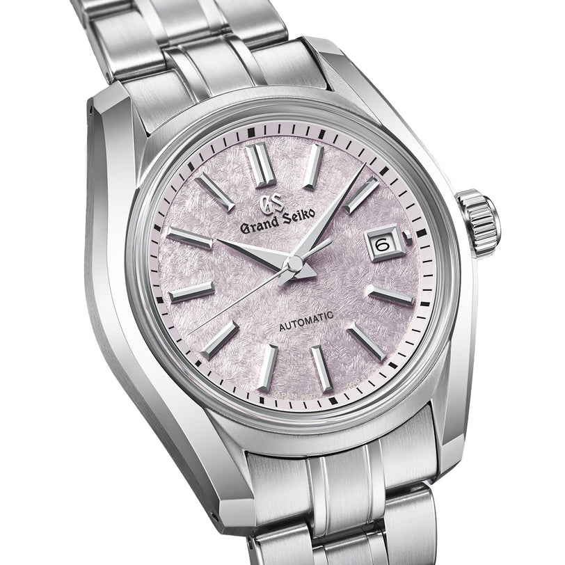 The Grand Seiko Ladies Automatic Heritage features a textured light pink cherry blossom-inspired dial, silver hour markers, date display at 3 o’clock, automatic mechanical movement, and a stainless steel bracelet.