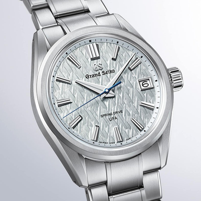 The Grand Seiko Spring Drive U.F.A Evolution 9 wristwatch features a silver case, textured white dial, date window, and blue second hand.