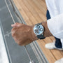 A person in a white shirt wearing an MB&F Legacy Machine Split Escapement EVO stands on a wooden and metal walkway, holding a cable.
