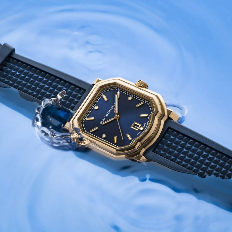 The Gerald Charles Maestro 2.0 Ultra-Thin, with an 18K Rose Gold 4N case, royal blue sunburst dial, and black textured strap, is partially submerged in water as ripples form around it.