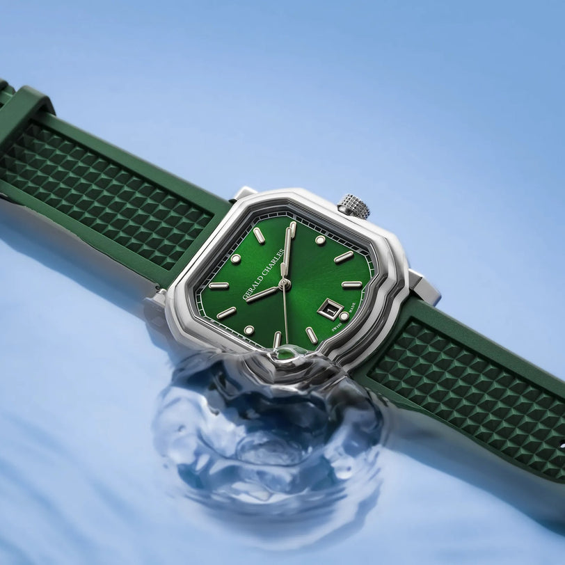 The Gerald Charles Maestro 2.0 Ultra-Thin features an emerald green sunburst dial with date display, a stainless steel case, and a matching vulcanised rubber strap, partially submerged in clear water.