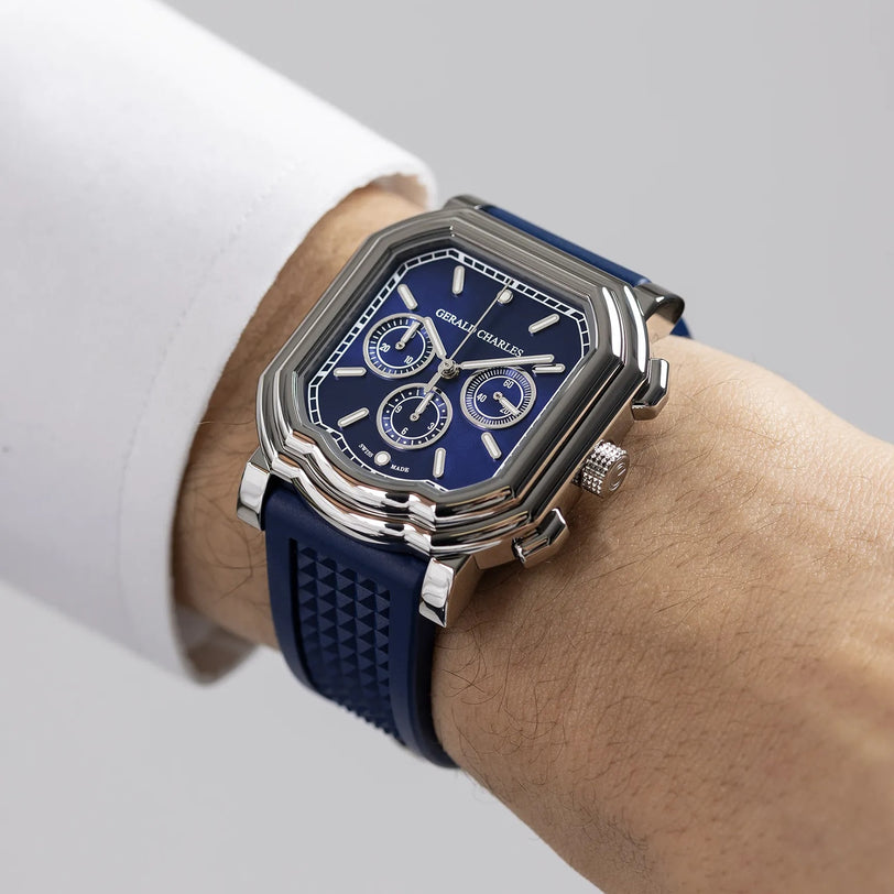 A person wears a Gerald Charles Maestro 3.0 Chronograph, featuring a silver case, blue face with Super-LumiNova details, and a blue rubber strap, on their left wrist against a plain background.