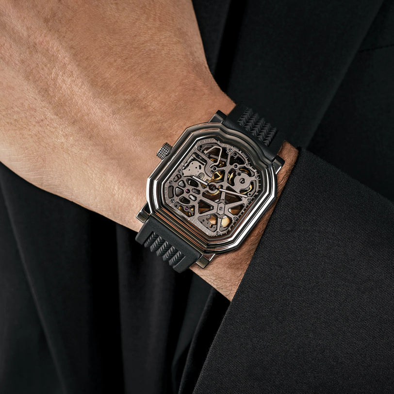A person wearing a black suit and the Gerald Charles Maestro 8.0 Squelette wristwatch with a skeleton dial and black rubber strap.