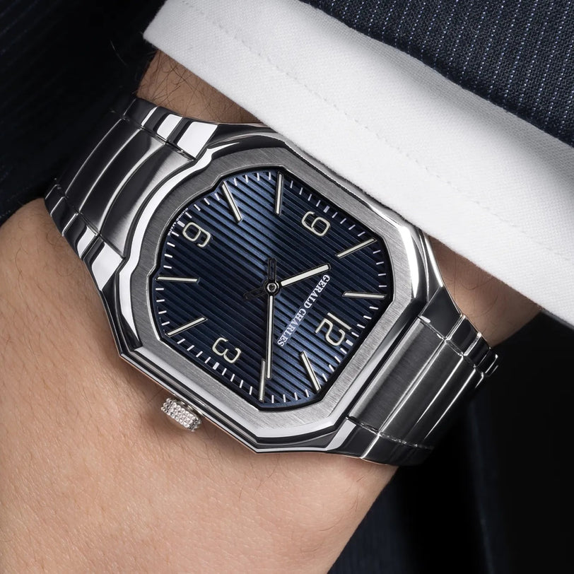 The Gerald Charles Masterlink Blue, a silver wristwatch with a blue dial and metal band, is worn on the wrist with a suit.