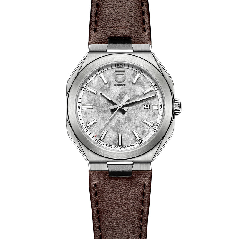 The ID Geneve Circular 1 - Mineral Grey is a silver wristwatch with a textured dial, brown leather strap, and date window at 3 o’clock.