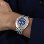 The DOXA Sub 300T Caribbean, featuring a stainless steel band and blue dial, is worn on a persons left wrist against a dark blue sleeve.