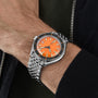 A person wearing the DOXA Sub 200 Professional diver’s watch with an orange dial, 316L stainless steel band, and unidirectional rotating bezel on their left wrist, dressed in a dark jacket and green shirt.