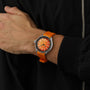 A person wearing the DOXA Sub 200 Professional divers watch with an orange strap and dial, featuring a unidirectional rotating bezel, is dressed in a black jacket with a visible zipper.