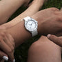 Someone wearing a DOXA Sub 200 Whitepearl, a white divers watch with an orange dial, sits cross-legged on the grass; another person’s arms and legs are partly visible nearby.