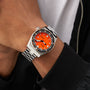A person wearing a DOXA Sub 600T Professional dive watch with a silver bracelet, orange dial, and black bezel, dressed in a black jacket and white shirt.