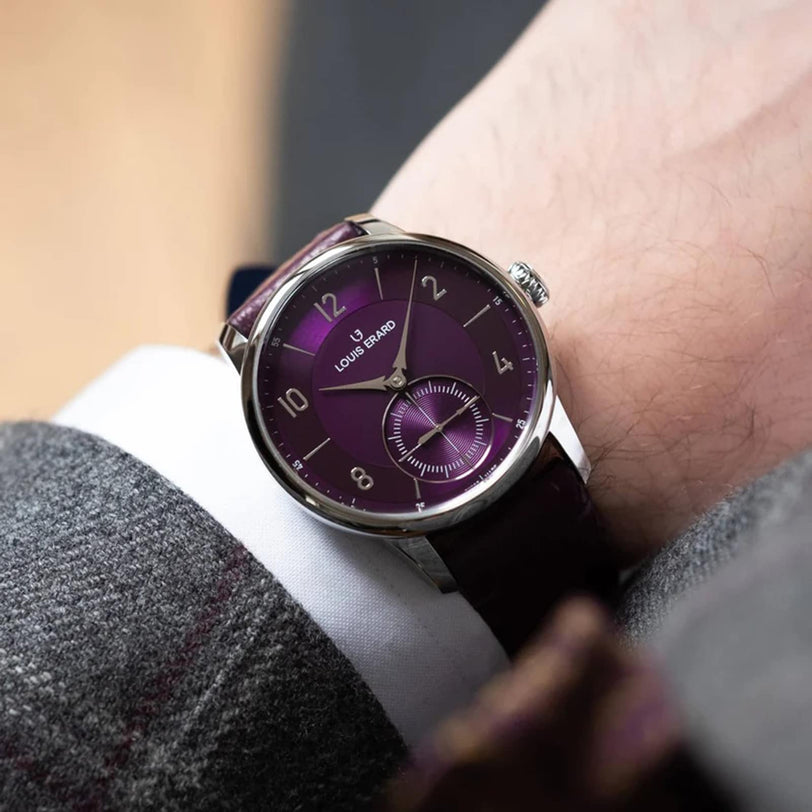 A person wearing a Louis Erard Petite Seconde Violette wristwatch with a purple dial and silver case.