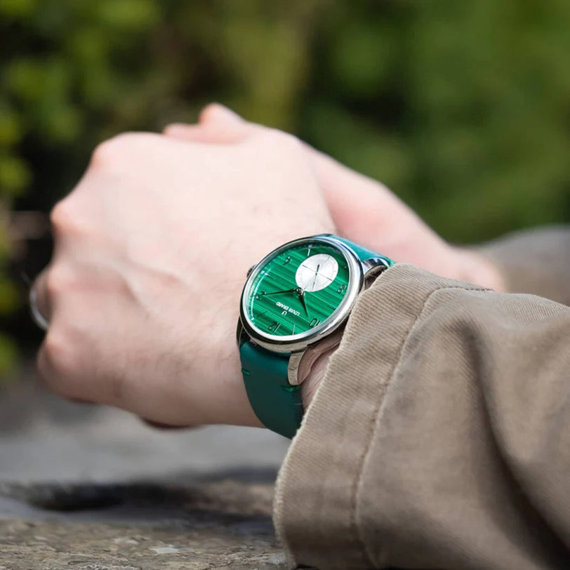 A person wearing the Louis Erard Petite Seconde Malachite wristwatch with a silver case and green strap, hands clasped, outdoors.