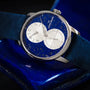 The Louis Erard Régulateur Lapis-Lazuli wristwatch features a striking blue face with dual subdials, shown here resting on a dark blue surface.