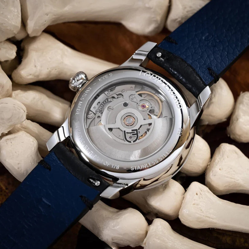 The La Petite Seconde Louis Horror x seconde/seconde/ watch by Louis Erard, featuring a blue strap and exposed movement, rests atop a pile of white bones.