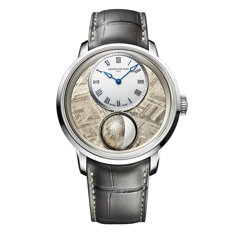 The Arnold & Son Luna Magna Platinum is a luxury wristwatch featuring a gray leather strap, Roman numeral dial, and decorative textured silver details.
