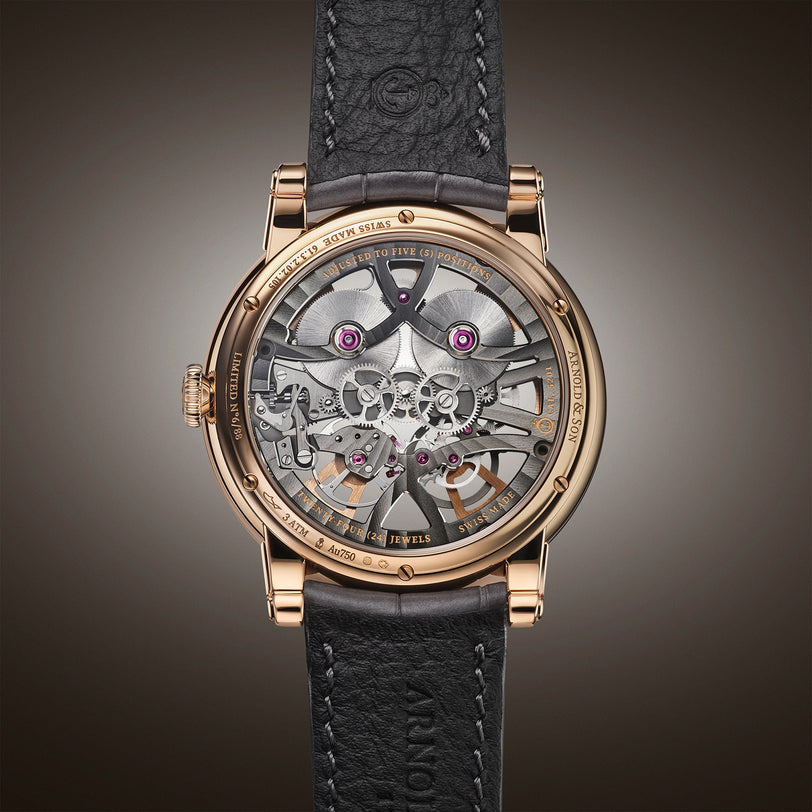 The Arnold & Son Nebula 41.5 Red Gold is a luxury watch featuring a transparent back that reveals intricate gears and mechanisms, paired with a black leather strap.