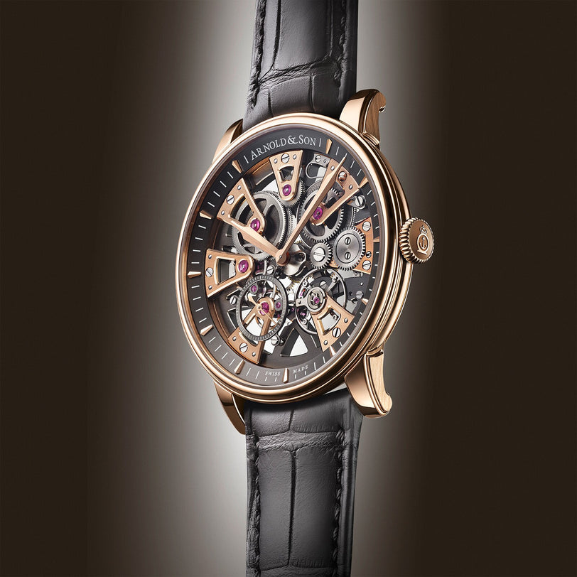 The Arnold & Son Nebula 41.5 Red Gold is a luxury skeleton watch with a black leather strap and a red gold case, elegantly displaying its intricate inner mechanisms.