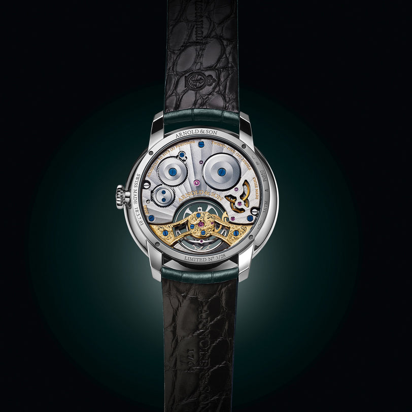 The Arnold & Son Ultrathin Tourbillon Platinum features an exposed movement with visible intricate gears and a sleek black leather strap.