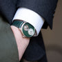 A person wearing the Arnold & Son Ultrathin Tourbillon Platinum, a green luxury watch with visible tourbillon, hand in pocket and dressed in a suit.