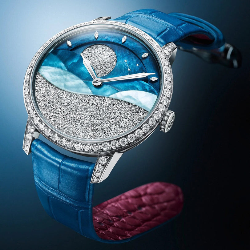 The Arnold & Son Perpetual Moon 38 White Gold Mintnight is a luxury watch featuring a blue strap, diamond bezel, and a moonlit landscape design on the dial.