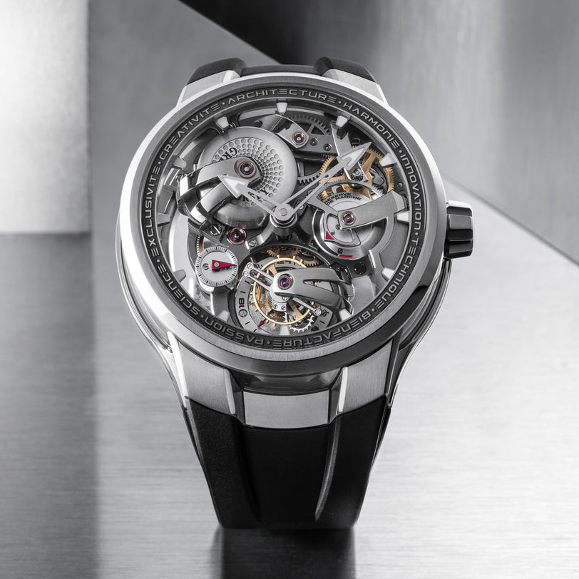 A close-up of the Greubel Forsey Tourbillon 24 Secondes Architecture, featuring its exposed mechanical movement, visible gears, and black strap against a metallic background—showcasing its architectural tourbillon design.
