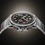The Angelus Chronodate Titanium Black Titanium wristwatch features a black dial, gold accents, and chronograph functions, showcased against a dark gradient background.