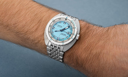 A wrist wears the DOXA Sub 300 watch with a light blue dial and silver-tone strap