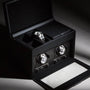 The WOLF Axis Double Watch Winder With Storage, shown in black and illuminated by dramatic lighting, elegantly displays two luxury watches.