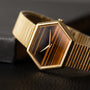The Piaget Hexagonal Tigers Eye gold wristwatch with a brown striped face is displayed on a black textured surface.