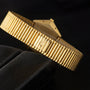 The Piaget Hexagonal Tigers Eye gold watch with a textured metal band is displayed on a black surface.