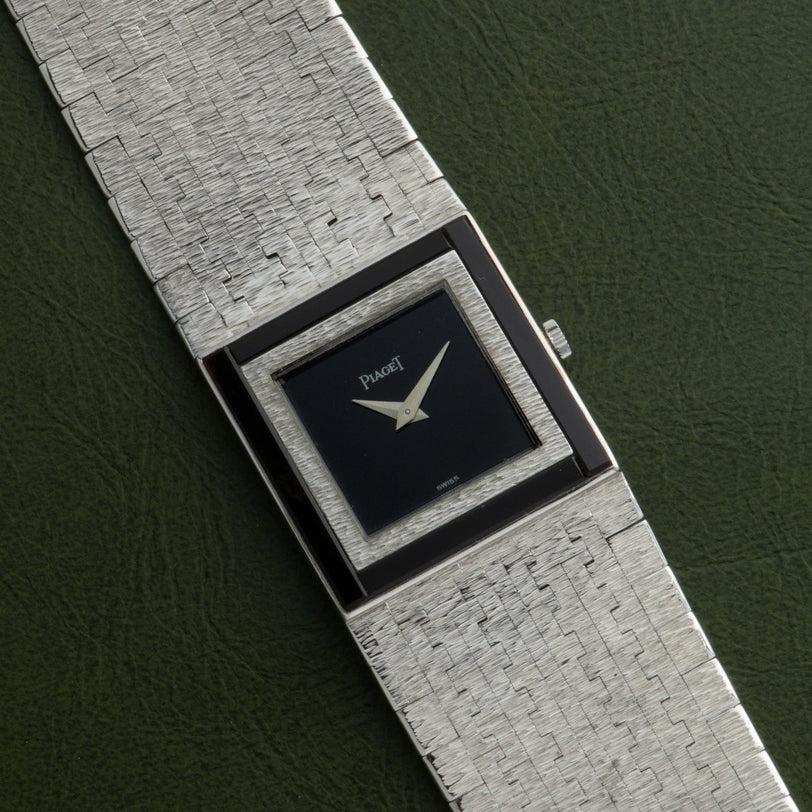 A Piaget white gold Onyx dress watch with a textured band and black square face on a green background.