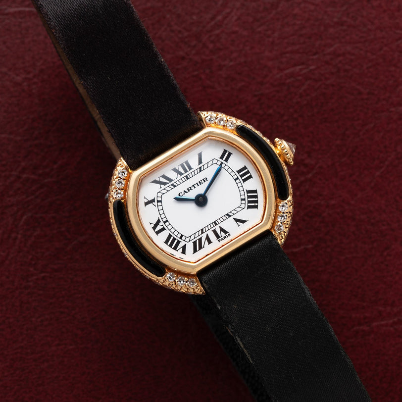 Cartier Ellipse watch featuring a black strap, gold case, diamond accents, and Roman numerals on a burgundy dial.