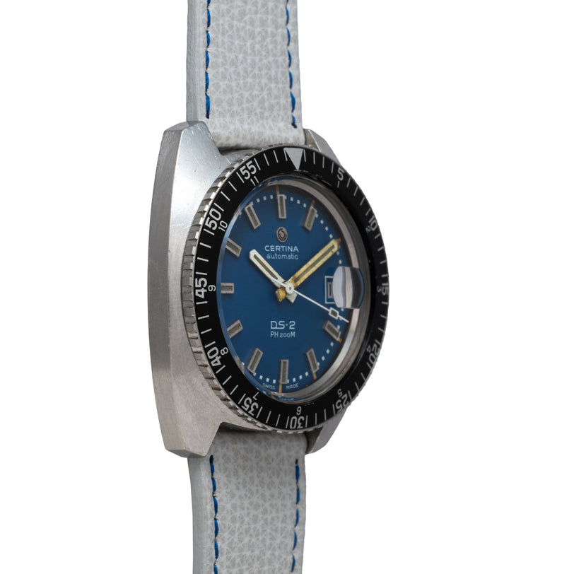 Certina DS-2 automatic watch with blue dial, black bezel, gold hands, and gray fabric strap with blue stitching.