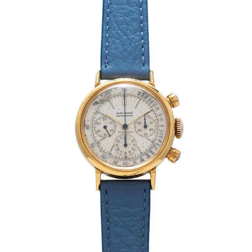 Gold-tone Movado chronograph watch with cream dial, subdials, and blue leather strap.