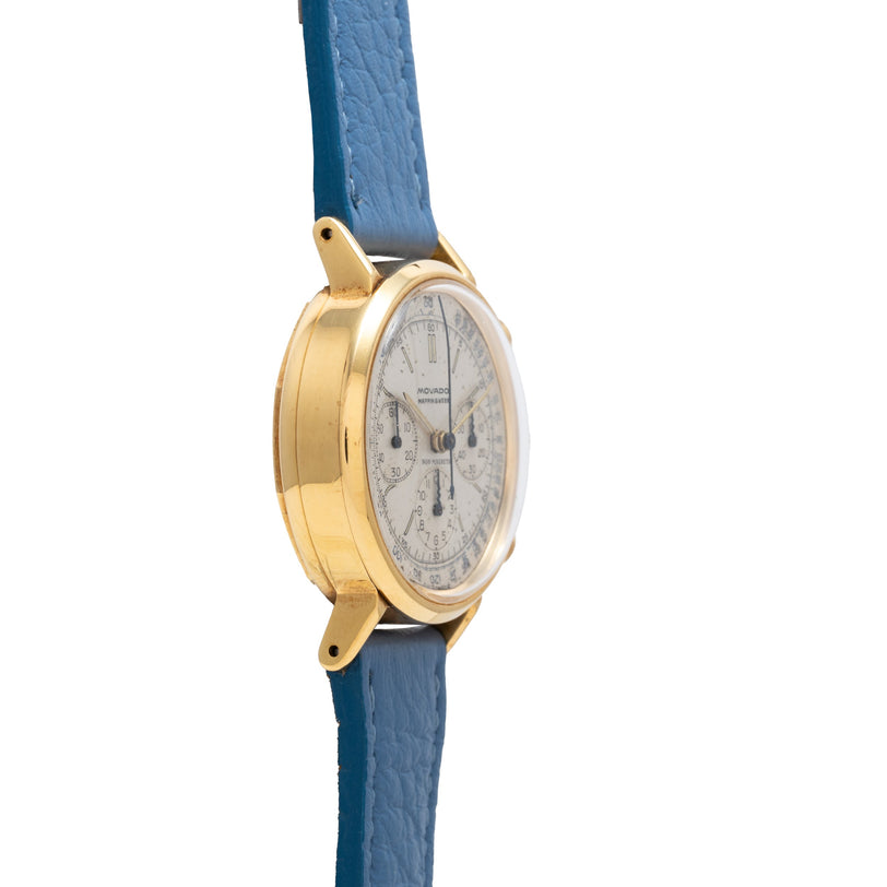 Gold-tone Movado chronograph watch with cream dial and blue leather strap.